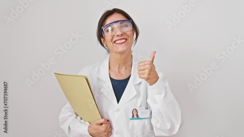 Cheerful mature hispanic woman giving a cool 'okay' sign! sportin' safety glasses, holding a clipboard, confidently showing approval on an isolated white background. exuding positive vibes! photo