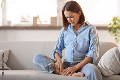 Young european pregnant lady in homewear massaging swollen foot indoor photo