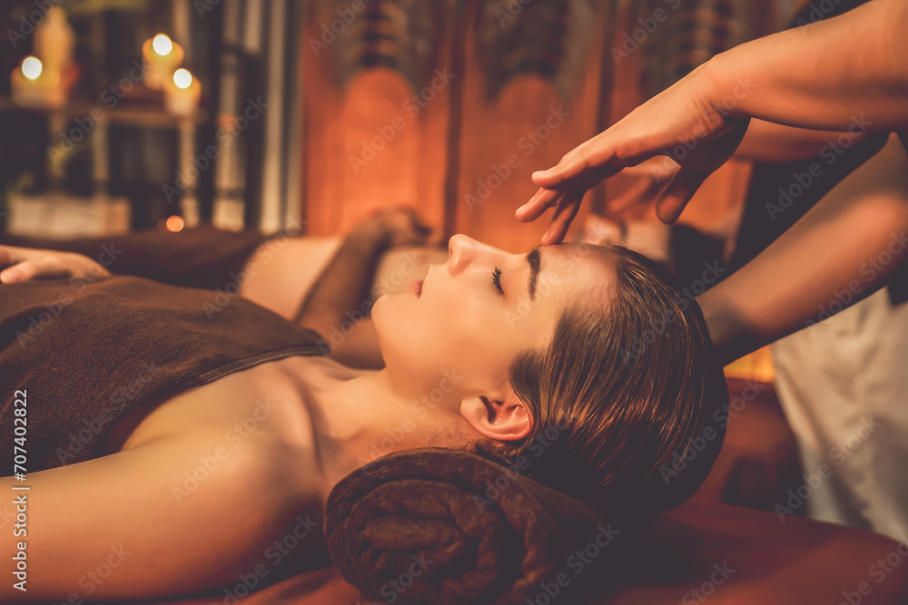 Couple customer enjoying relaxing anti-stress head massage and pampering facial beauty skin recreation leisure in warm candle lighting ambient salon spa in luxury resort or hotel. Quiescent - obrazy, fototapety, plakaty 