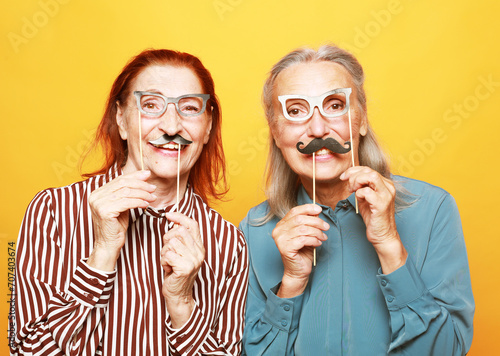 funny elderly female friends with fake mustache and glasses, laughs and prepares for party photo