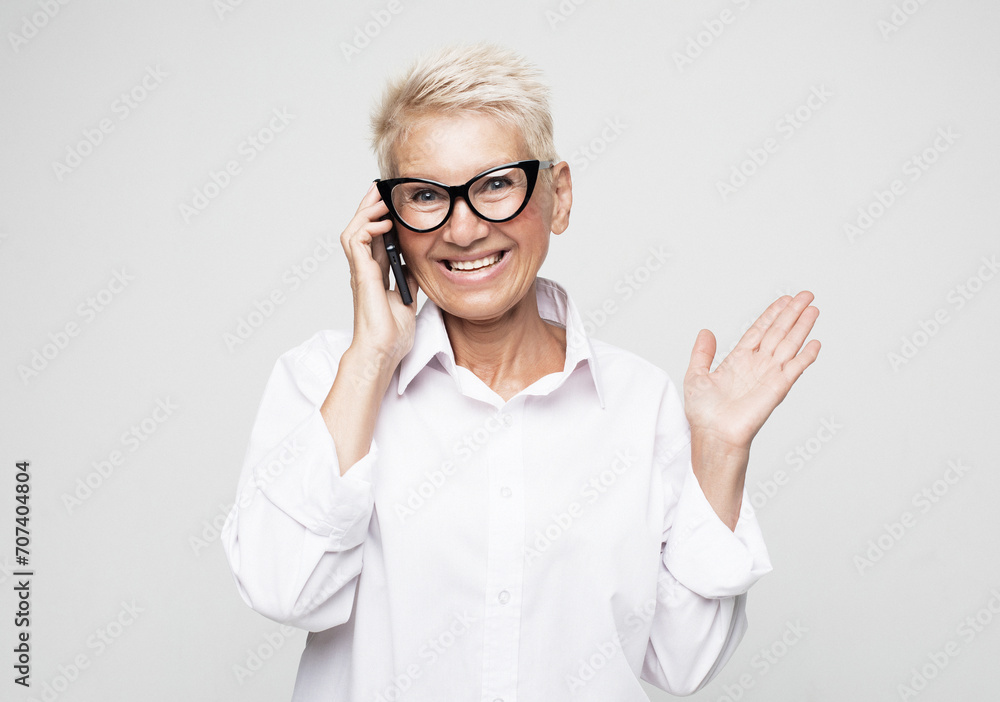 Surprised aged woman using phone, isolated over grey background. Surprised aged woman using phone, isolated over grey background.