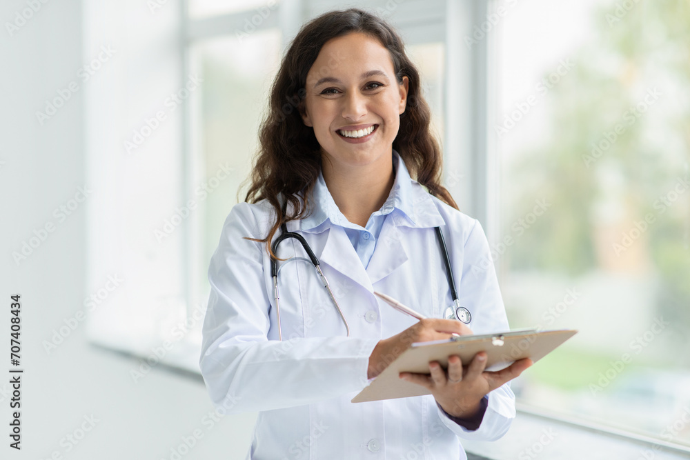 Positive young woman doctor taking notes in clipboard Positive young woman doctor taking notes in clipboard
