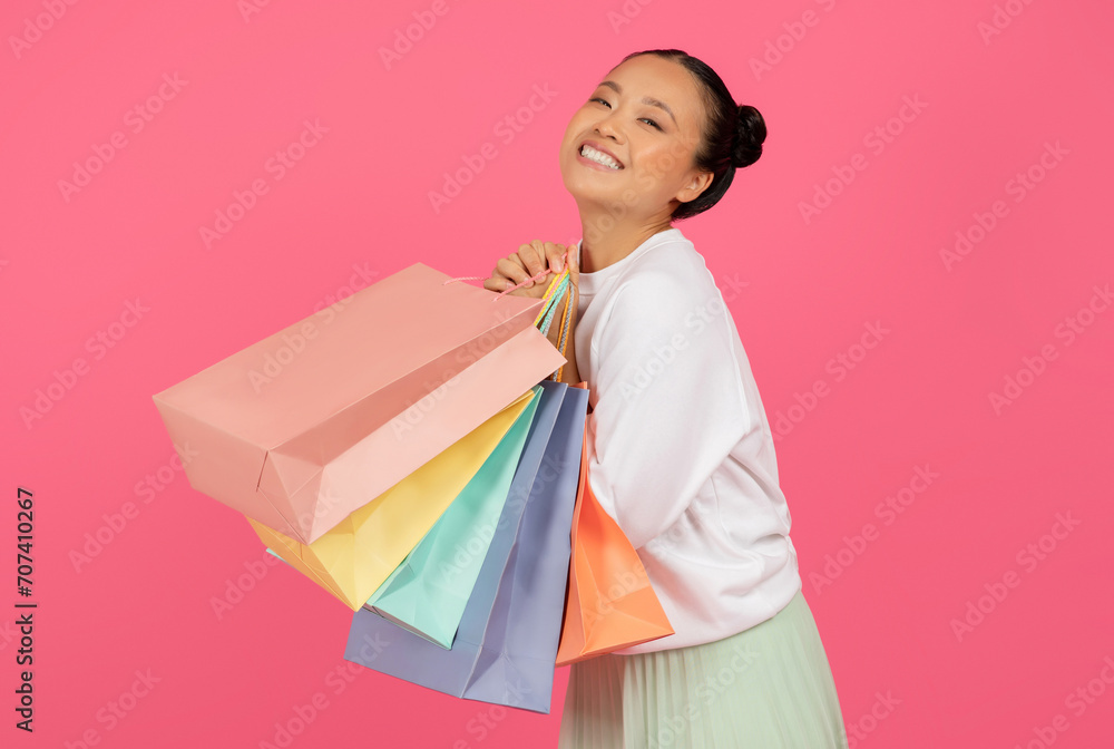 Happy young asian woman clutching vibrant paper shopping bags Happy young asian woman clutching vibrant paper shopping bags