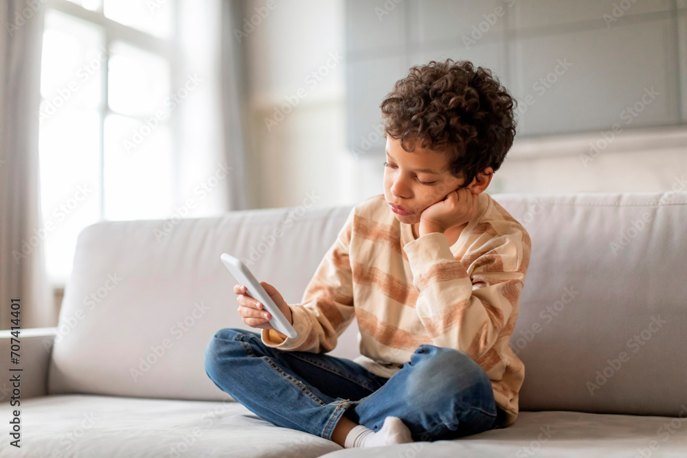 Upset Black Boy Using Mobile Phone While Relaxing On Couch At Home Upset Black Boy Using Mobile Phone While Relaxing On Couch At Home