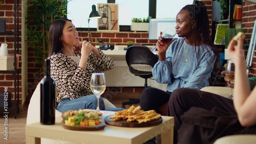 BIPOC BFFs talking, drinking wine at reunion gathering, gossiping about their husbands. Asian, african american and caucasian girls enjoying social life at apartment party in living room photo