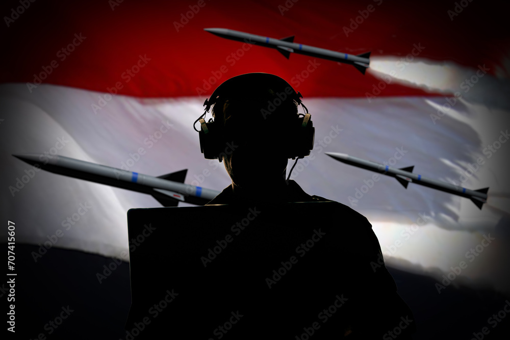 Silhouette of a military man wearing headphones behind a laptop against a background of the Yemeni flag and flying missiles, contour lighting.  - obrazy, fototapety, plakaty 
