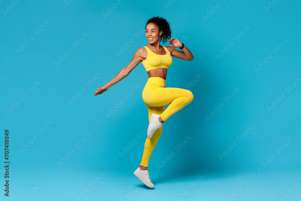 black woman in sportswear jumping doing exercise on blue backdrop