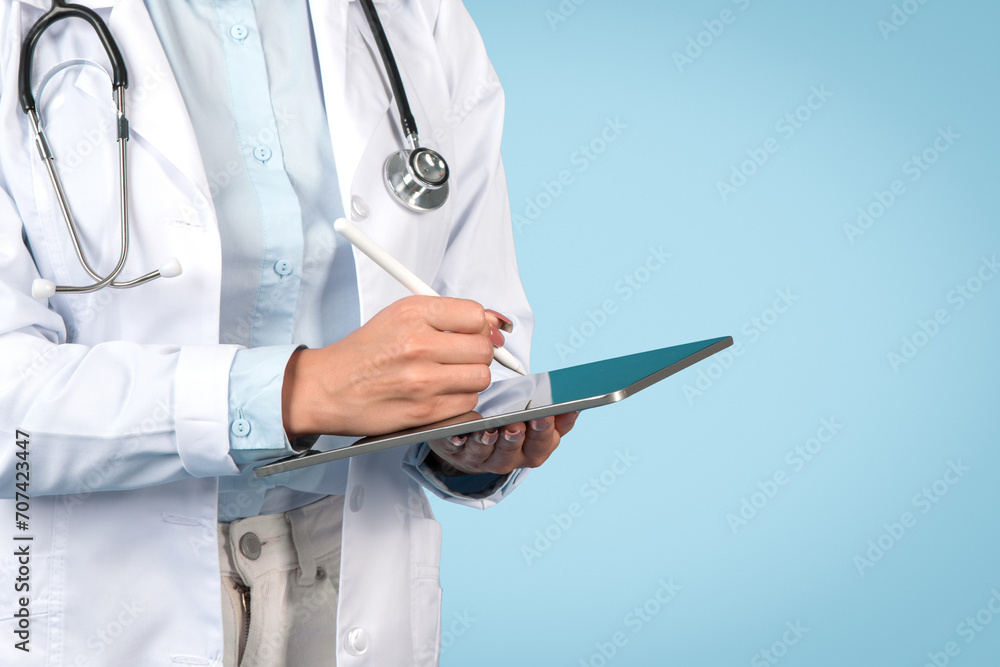 Woman doctor writing on tablet, close-up, blue background Woman doctor writing on tablet, close-up, blue background