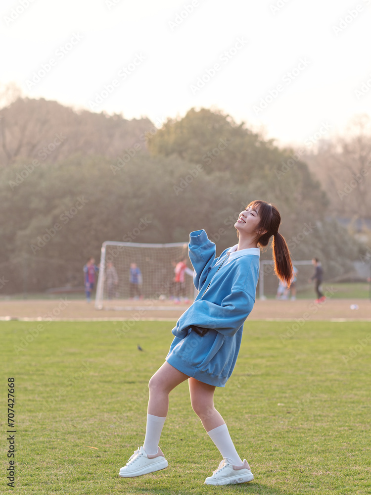 Beautiful young Chinese woman posing on green grass field in sunny summer day, wearing blue loose oversized top, mini skirt and white shoes. Emotions, people, beauty, youth and lifestyle portrait.