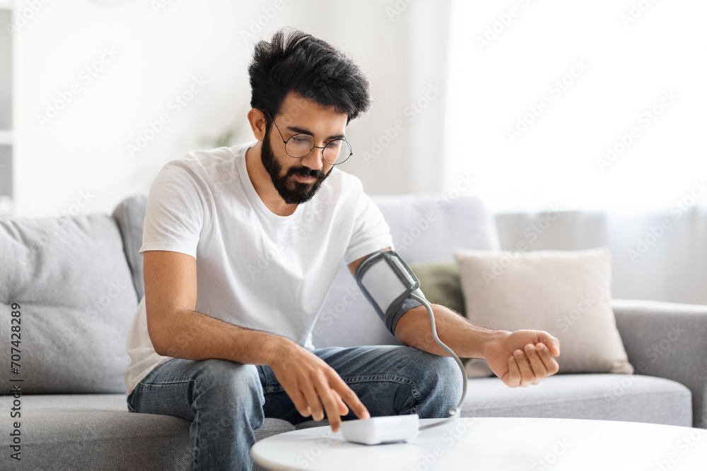 Concentrated Indian man monitoring his blood pressure with a digital sphygmomanometer Concentrated Indian man monitoring his blood pressure with a digital sphygmomanometer