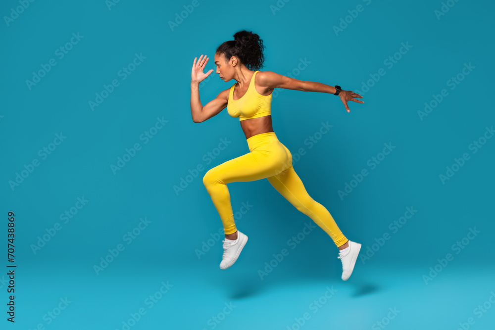 Athletic black woman leaping during dynamic workout on blue backdrop