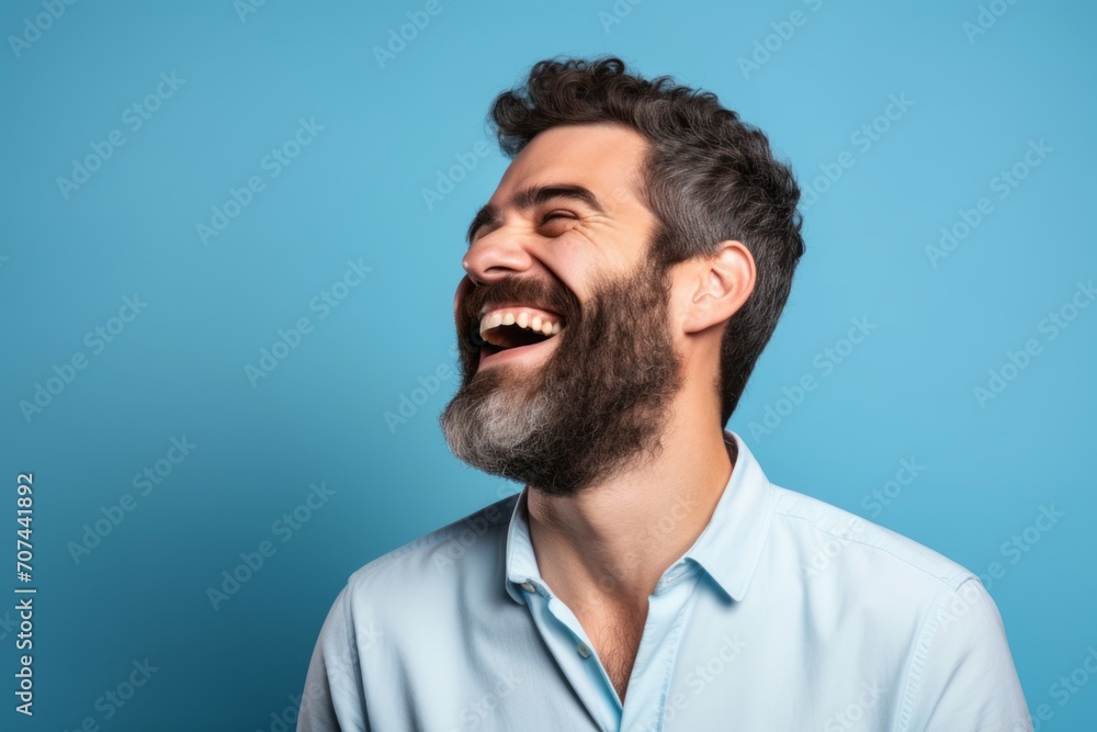 Handsome man with long beard laughing and looking up on blue background Handsome man with long beard laughing and looking up on blue background