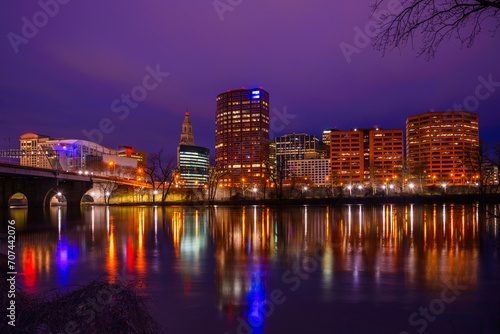 Hartford Skyline at night over the Connecticut River  a vibrant cityscape along Riverfront Park  lighted Riverwalk trail  and Founders Bridge in the capital city of Connecticut State  United States