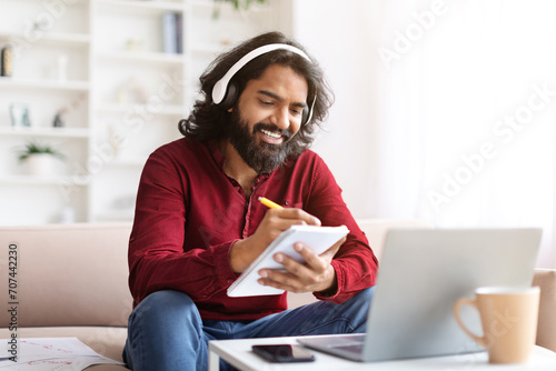 Joyful indian guy have online training at home, using laptop photo