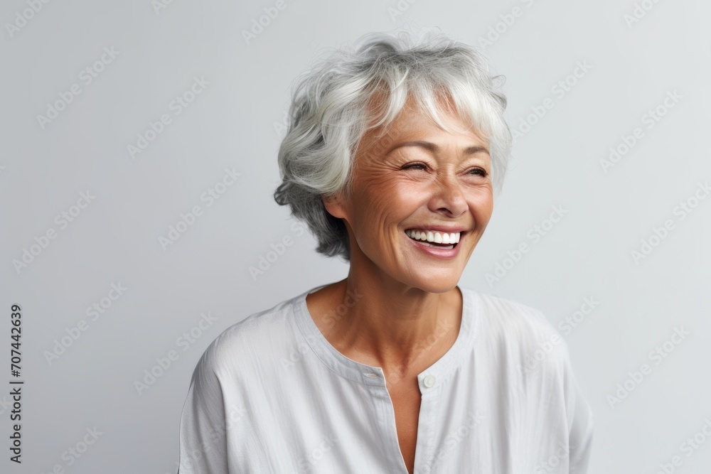 Portrait of a happy senior woman smiling at the camera against grey background Portrait of a happy senior woman smiling at the camera against grey background