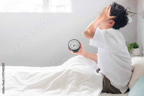 目覚まし時計を見て朝起床する男性（睡眠・覚醒・眠り）
 photo