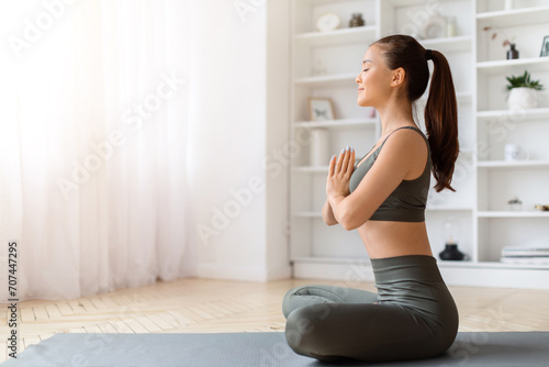 Tranquil young asian woman meditating at home, practicing yoga with clasped arms