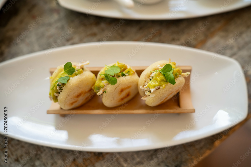 small corn cake arepas filled with chicken avocado guacamole and topped with leaves at a latin restaurant during the day small corn cake arepas filled with chicken avocado guacamole and topped with leaves at a latin restaurant during the day