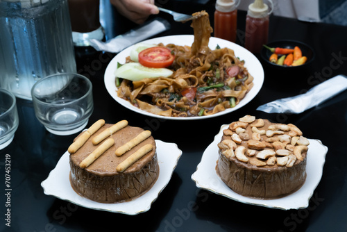A photo of a hand enjoying a meal with a menu of Kwetiaw noodles, ice cream, water, and a milkshake on the table