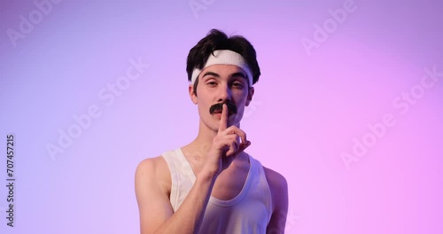 Poised 80s Caucasian man confidently signals 'Shh' with a hush gesture against a stylish purple background. This scene captures the retro sophistication of silent assurance. photo