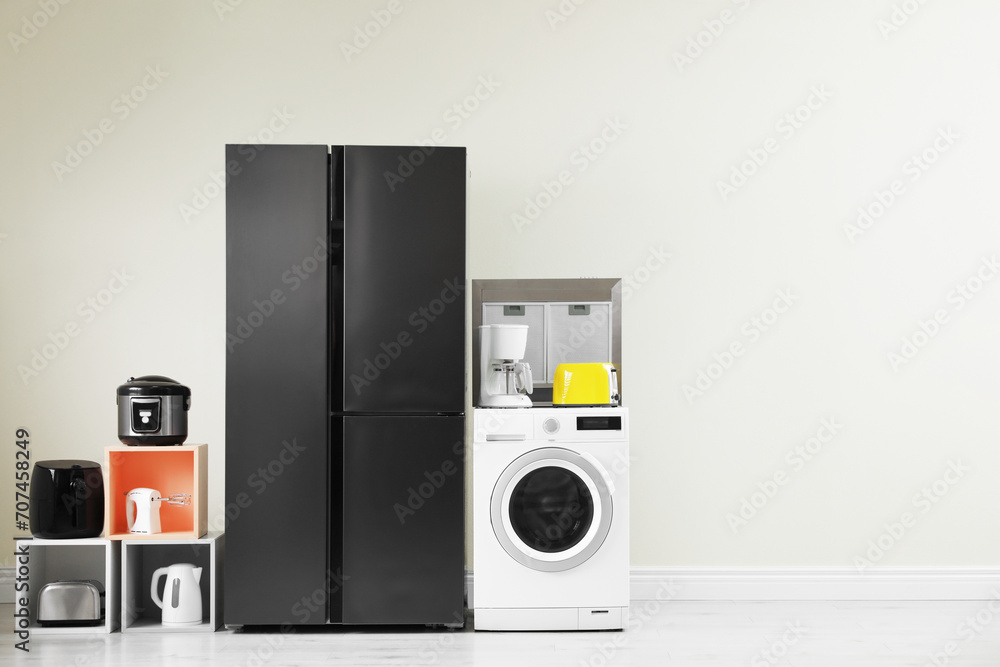 Modern refrigerator and other household appliances near beige wall indoors, space for text Modern refrigerator and other household appliances near beige wall indoors, space for text