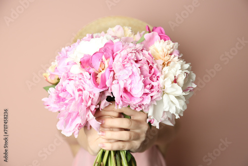 Woman with bouquet of beautiful peonies on beige background, closeup