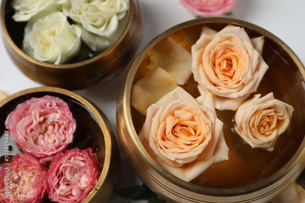 Tibetan singing bowls with water and different beautiful rose flowers on white background, above view Tibetan singing bowls with water and different beautiful rose flowers on white background, above view