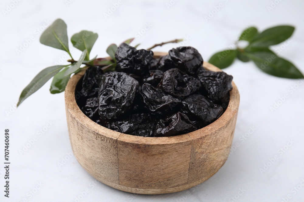 Sweet dried prunes in bowl and green leaves on white table, closeup Sweet dried prunes in bowl and green leaves on white table, closeup