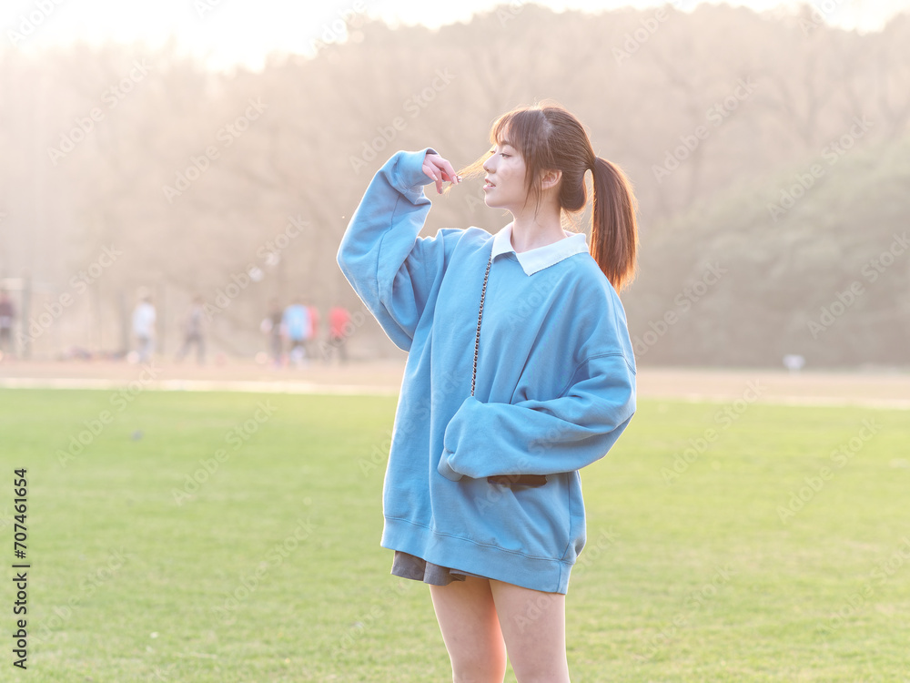 Beautiful young Chinese woman posing on green grass field in sunny summer day, wearing blue loose oversized top, mini skirt and white shoes. Emotions, people, beauty, youth and lifestyle portrait. Beautiful young Chinese woman posing on green grass field in sunny summer day, wearing blue loose oversized top, mini skirt and white shoes. Emotions, people, beauty, youth and lifestyle portrait.