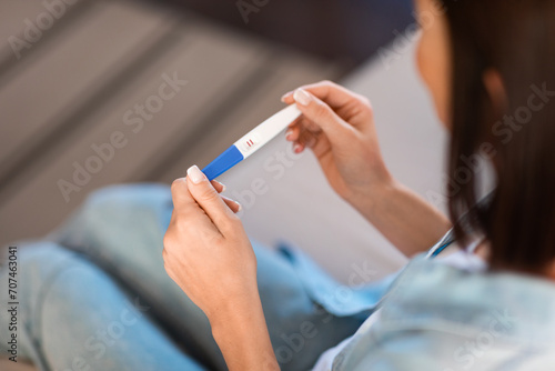 Unrecognizable young woman examines positive pregnancy test result sitting indoors