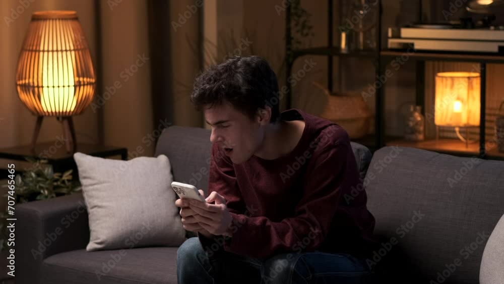 Seated on the sofa in the living room, a man, feeling bored, yawns while holding phone. The room becomes a backdrop for this moment of ennui, capturing a scene of monotony in the comfort of home. Seated on the sofa in the living room, a man, feeling bored, yawns while holding phone. The room becomes a backdrop for this moment of ennui, capturing a scene of monotony in the comfort of home.