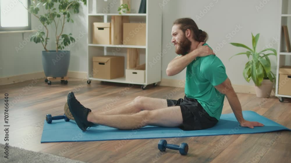 Young Man Sits on the Floor at Home, Got Injured in Training, Holding on His Shoulder, Rubbing the Bruised Area, Got a Sports Injury Young Man Sits on the Floor at Home, Got Injured in Training, Holding on His Shoulder, Rubbing the Bruised Area, Got a Sports Injury