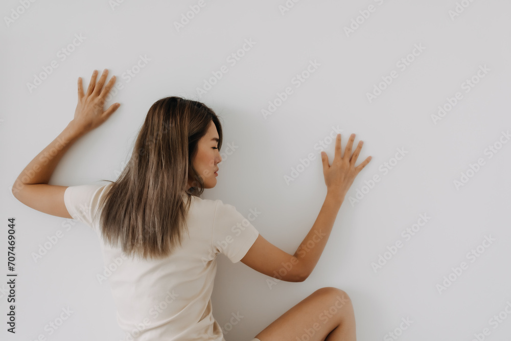 Funny asian woman lie on background try to spy and listen over the wall. Funny asian woman lie on background try to spy and listen over the wall.