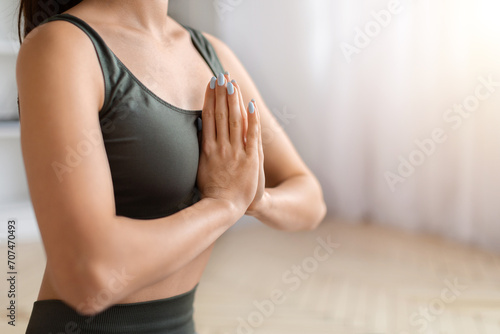 Cropped shot of sporty woman in activewear holding hands in namaste gesture