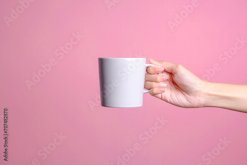 Woman hand holding white mug mockup on pink background 