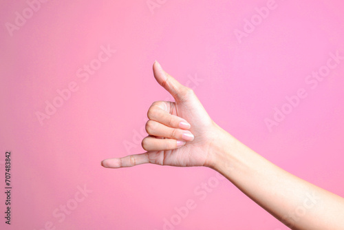 Woman hand showing calling hand gesture or shaka sign on pink background photo