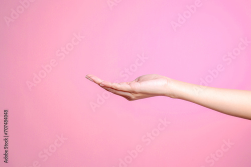 Hand showing palm up gesture isolated over pink pastel background, side view © Queenmoonlite Studio