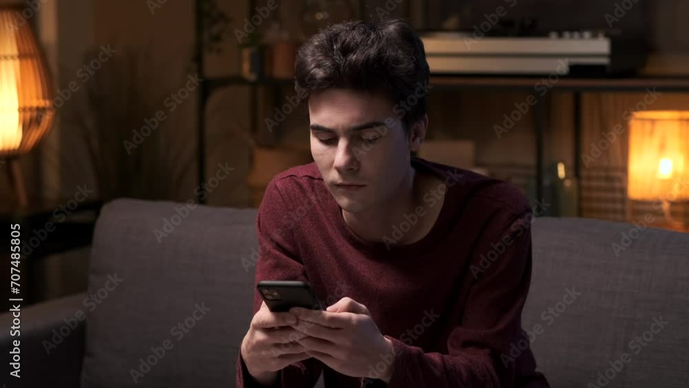 Man seated on the sofa engages in texting on phone. The soft glow of the room accentuates the relaxed atmosphere, creating a scene of modern connectivity and leisure within the living space. Man seated on the sofa engages in texting on phone. The soft glow of the room accentuates the relaxed atmosphere, creating a scene of modern connectivity and leisure within the living space.