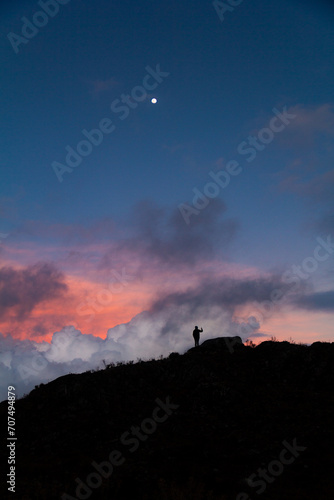 silhouette of person taking a photograph in mountain ridge at sunrise or sunset