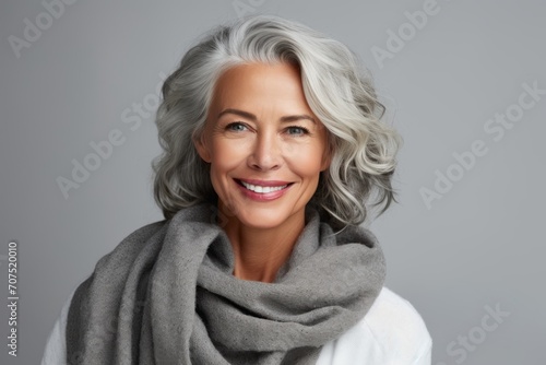 Portrait of a beautiful senior woman with grey scarf over grey background © Inigo
