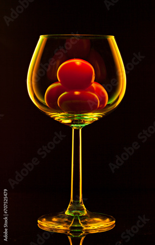 Wine glass with cherry tomatoes inside isolated on black background. 