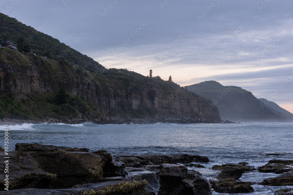 Ocean and mountain view with cloudy sky.