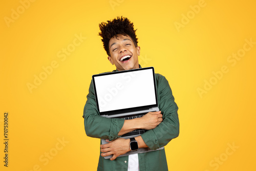 Overjoyed black guy hugging laptop with white blank screen photo