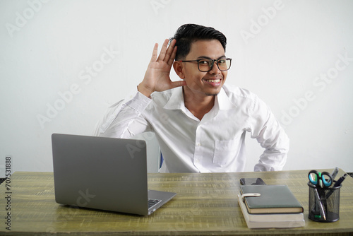 young asian businessman in a workplace listening to something by putting hand on the ear wearing white shirt isolated on white background photo