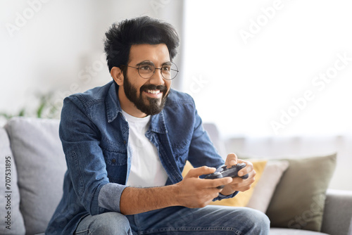 Cheerful young Indian man enjoying playing video games at home