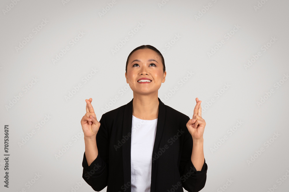 Happy young asian woman in suit crossed fingers, looking up at empty space Happy young asian woman in suit crossed fingers, looking up at empty space