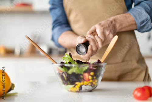 Focused elderly chef preparing nutritious vegetable salad, adding spices for flavor