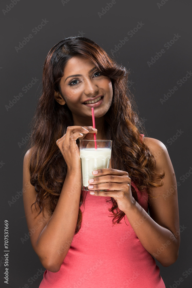 Indian Woman drinking glass of milk on grey background. Indian Woman drinking glass of milk on grey background.