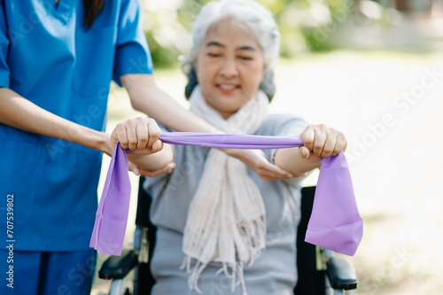 Asian physiotherapist helping elderly woman patient stretching arm during exercise correct with dumbbell in hand during training hand with patient Back problems in the garden.