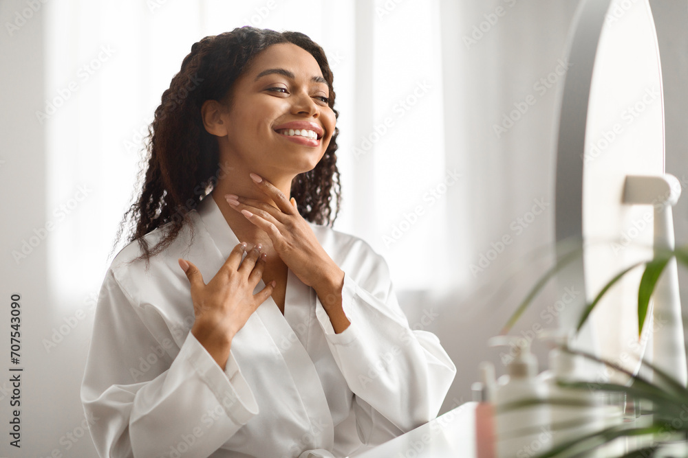 Beautiful black woman sitting at dressing table, touching skin on her neck Beautiful black woman sitting at dressing table, touching skin on her neck